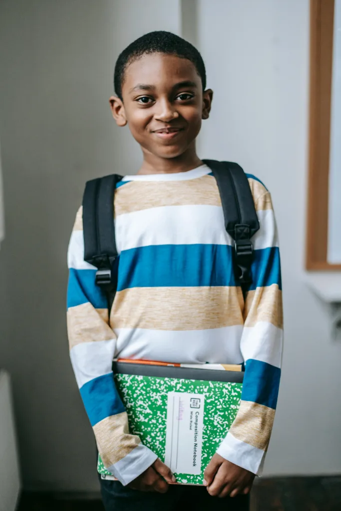 Child with backpack and books smiling at the camera
