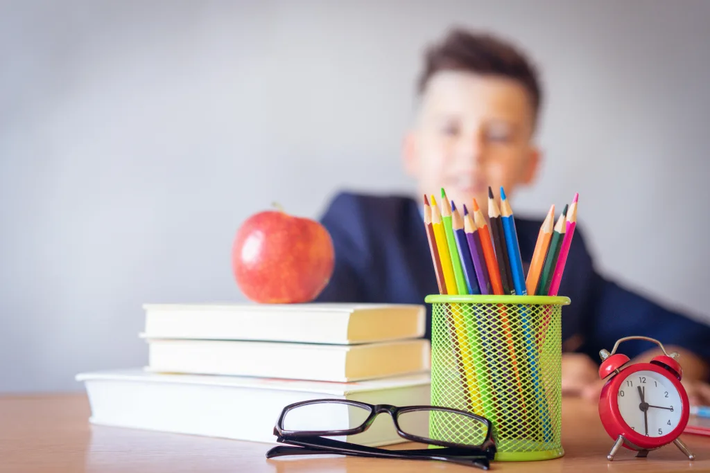 Child at desk with pens, books and an apple