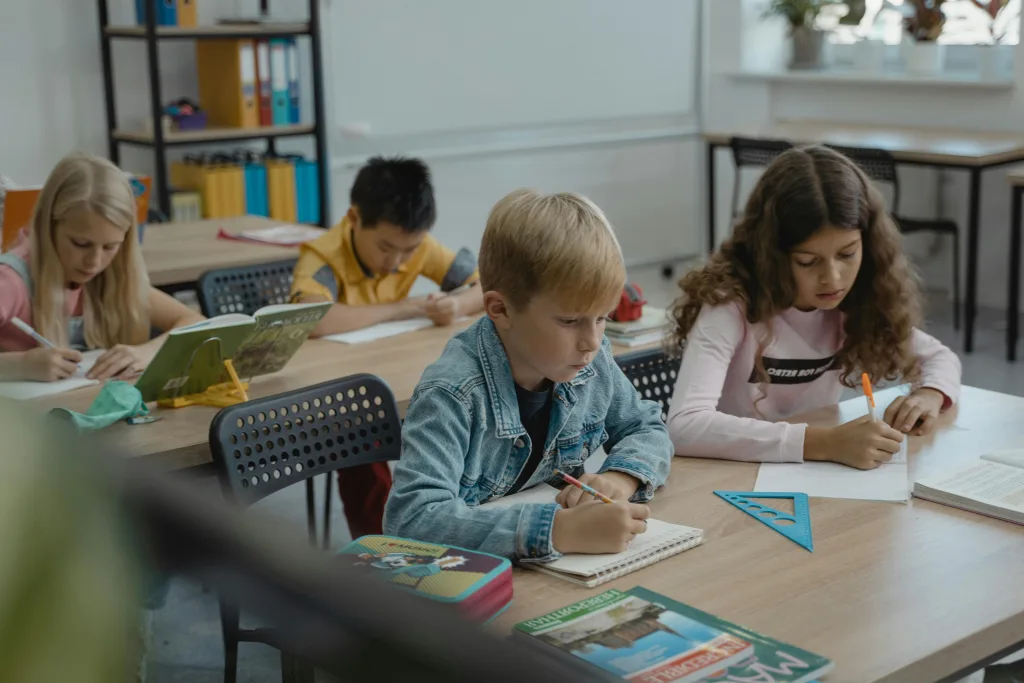 Children in classroom at desks with pen and paper