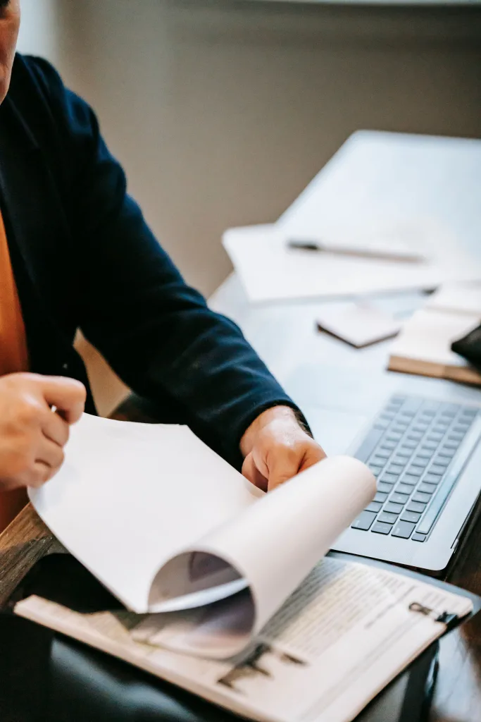 Person holding papers with laptop next to them